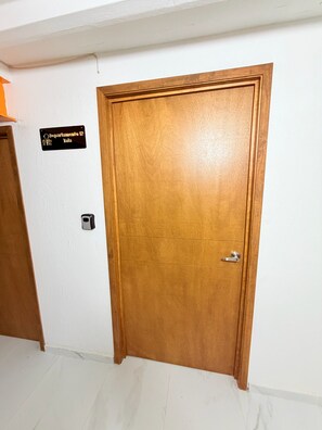 Una puerta de madera con un picaporte metálico, un letrero encima y un interruptor de luz en la pared.