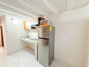Una cocina compacta con un refrigerador de acero inoxidable, un horno empotrado y un lavamanos.