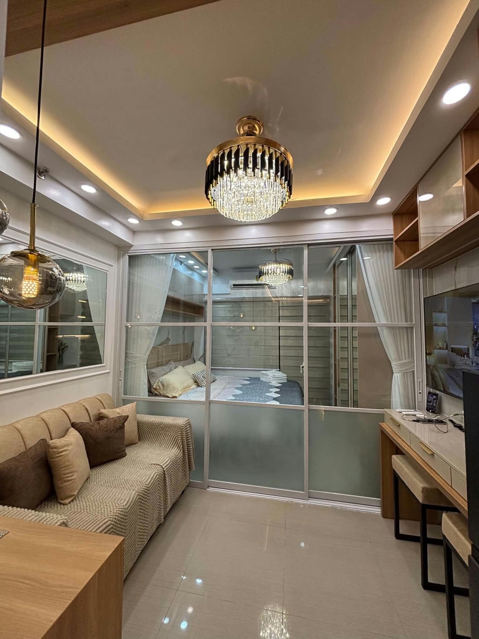A modern bedroom with a glass partition, a chandelier, a sofa, and a desk area.