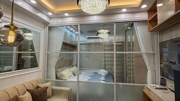 A modern bedroom with a glass partition, a chandelier, a sofa, and a desk area.