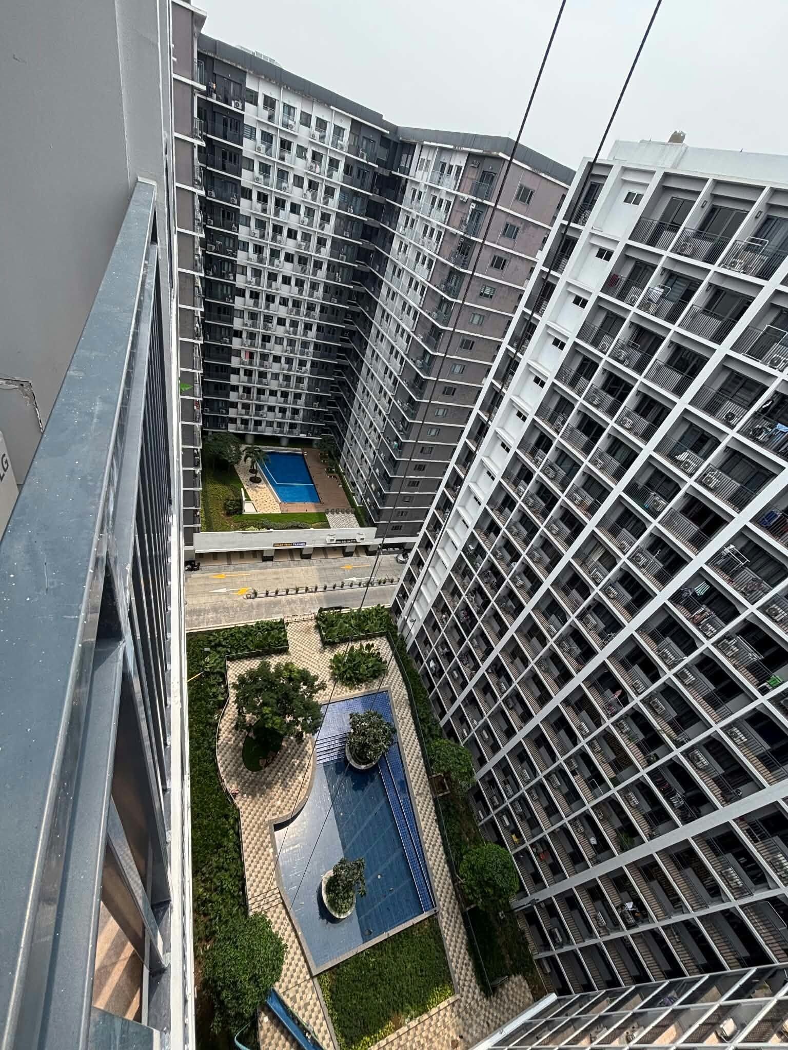 A high-rise residential building with multiple balconies, a central courtyard with a swimming pool, and a surrounding landscaped area.