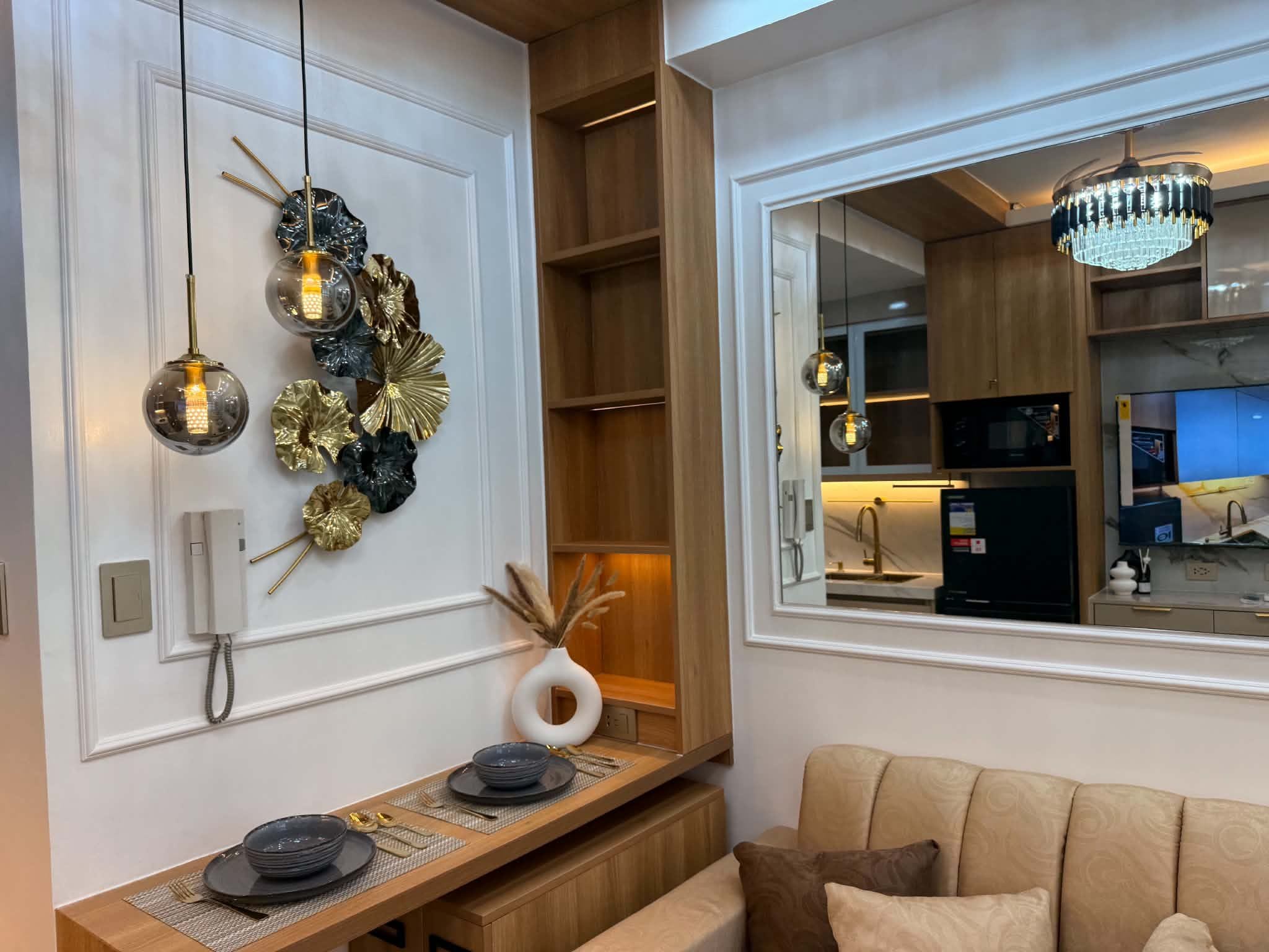 Un salon moderne avec un banc en bois, un élément décoratif mural et une vue sur la cuisine à travers une grande fenêtre.