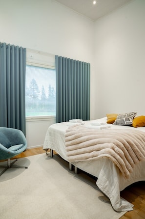 A bedroom with a bed, a chair, a window with curtains, and a view of buildings outside. - Nordic Design Villa, Sauna By Lapland Host (Rovaniemi)