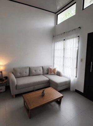 A living room with a sectional sofa, a wooden coffee table, and a lamp. - Casita Blanca /Great location with Mountain view (La Fortuna)