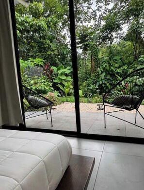 A bedroom with a large window, two black wireframe chairs, and a white bed. - Casita Blanca /Great location with Mountain view (La Fortuna)