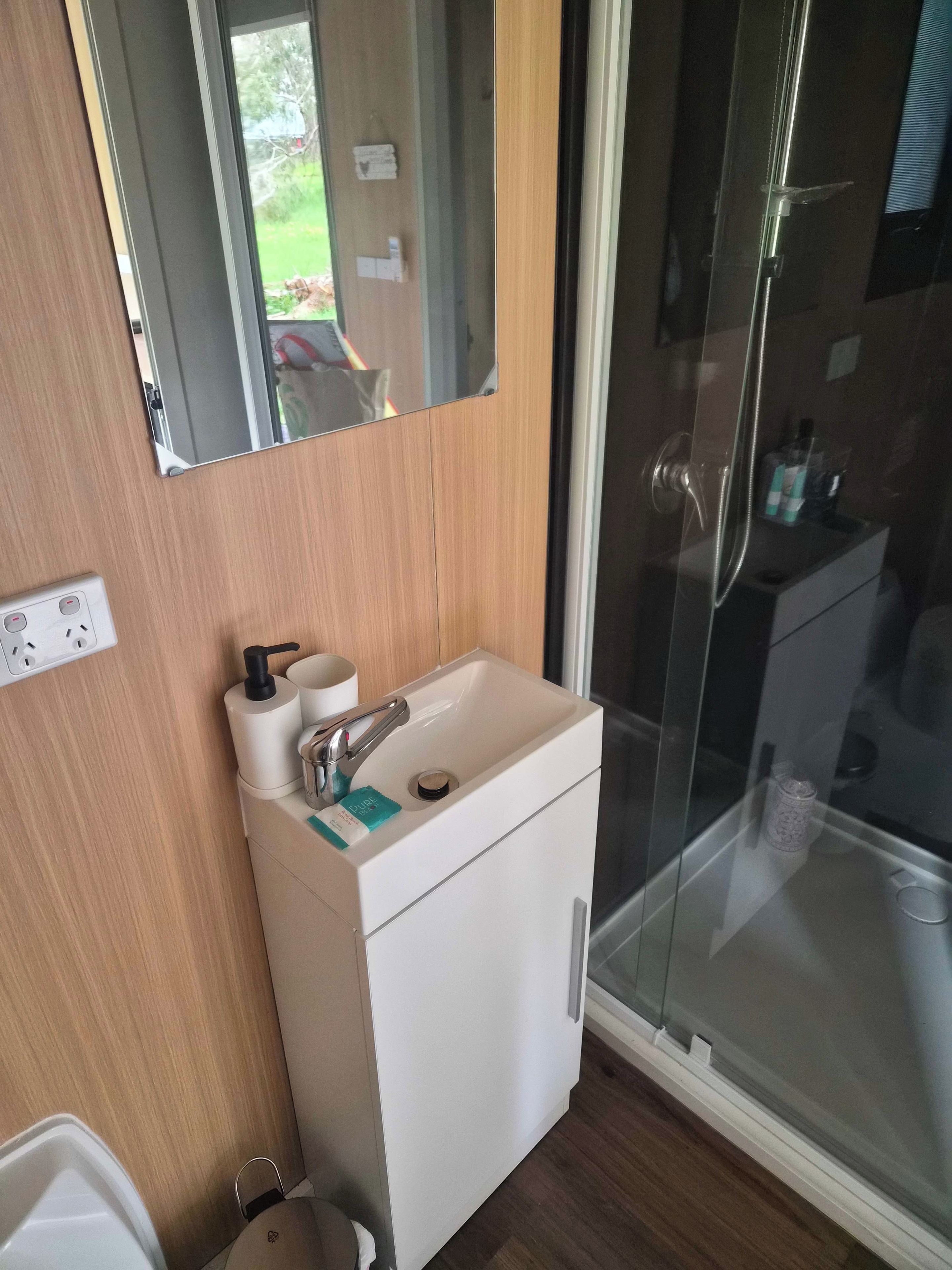 A bathroom with a white sink, a mirror, a glass shower enclosure, and a wooden wall.