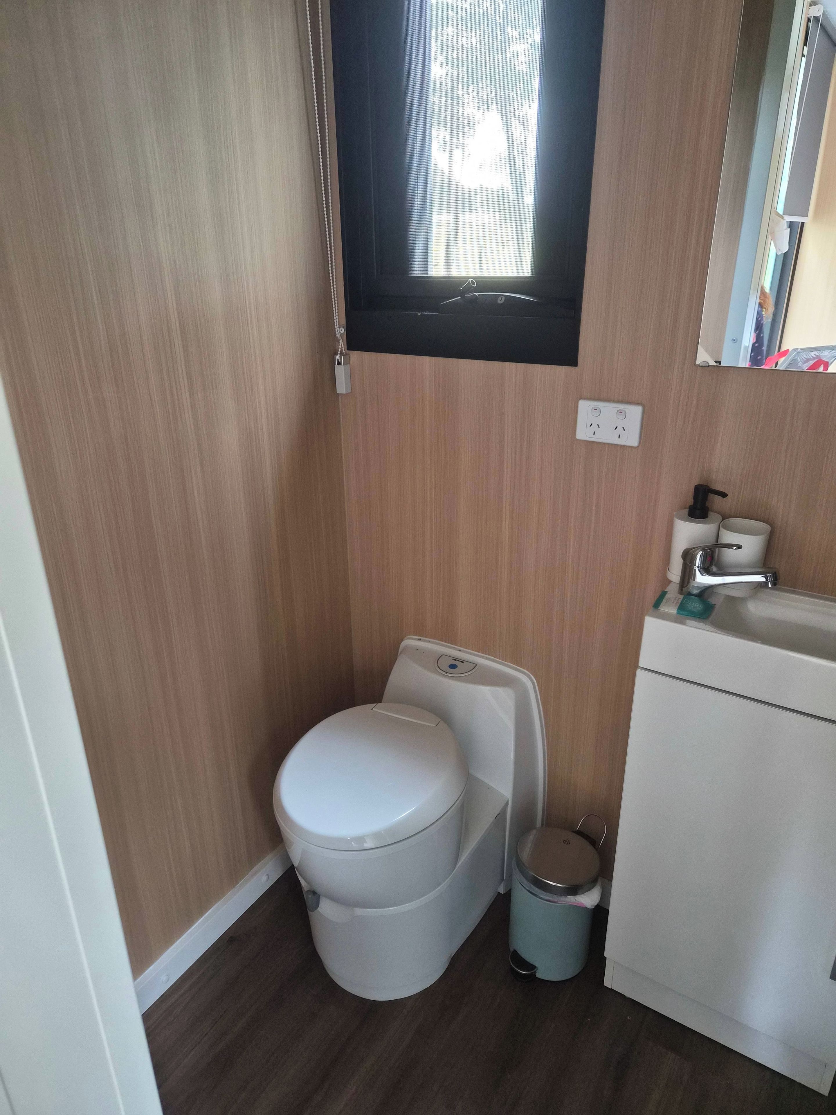 Een kleine badkamer met toilet, prullenbak en wastafel.