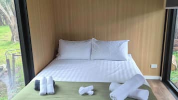 Ett hotellrum med en säng, ett grönt sängöverkast, vita kuddar och hoprullade handdukar.
