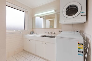 A bathroom with a double sink, a mirror, a washing machine, and a window. - Calendo Apartments  Unit 05 (Merimbula)