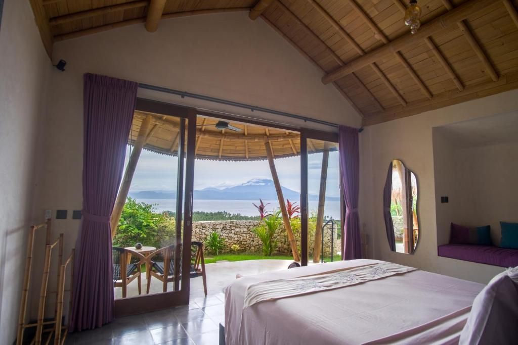 A bedroom with a large bed, a view of a mountainous landscape, and a balcony with a table and chairs.