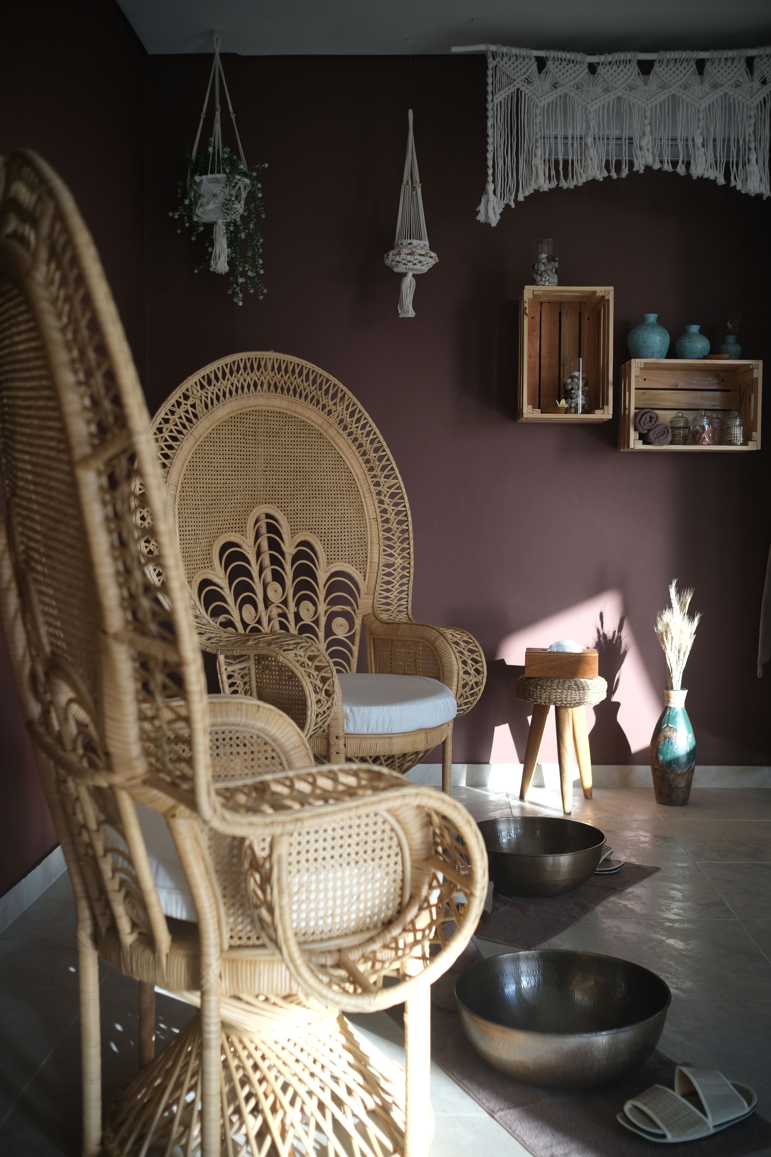 A wicker chair with a cushion, a wooden side table with a bowl, and a macramé wall hanging.