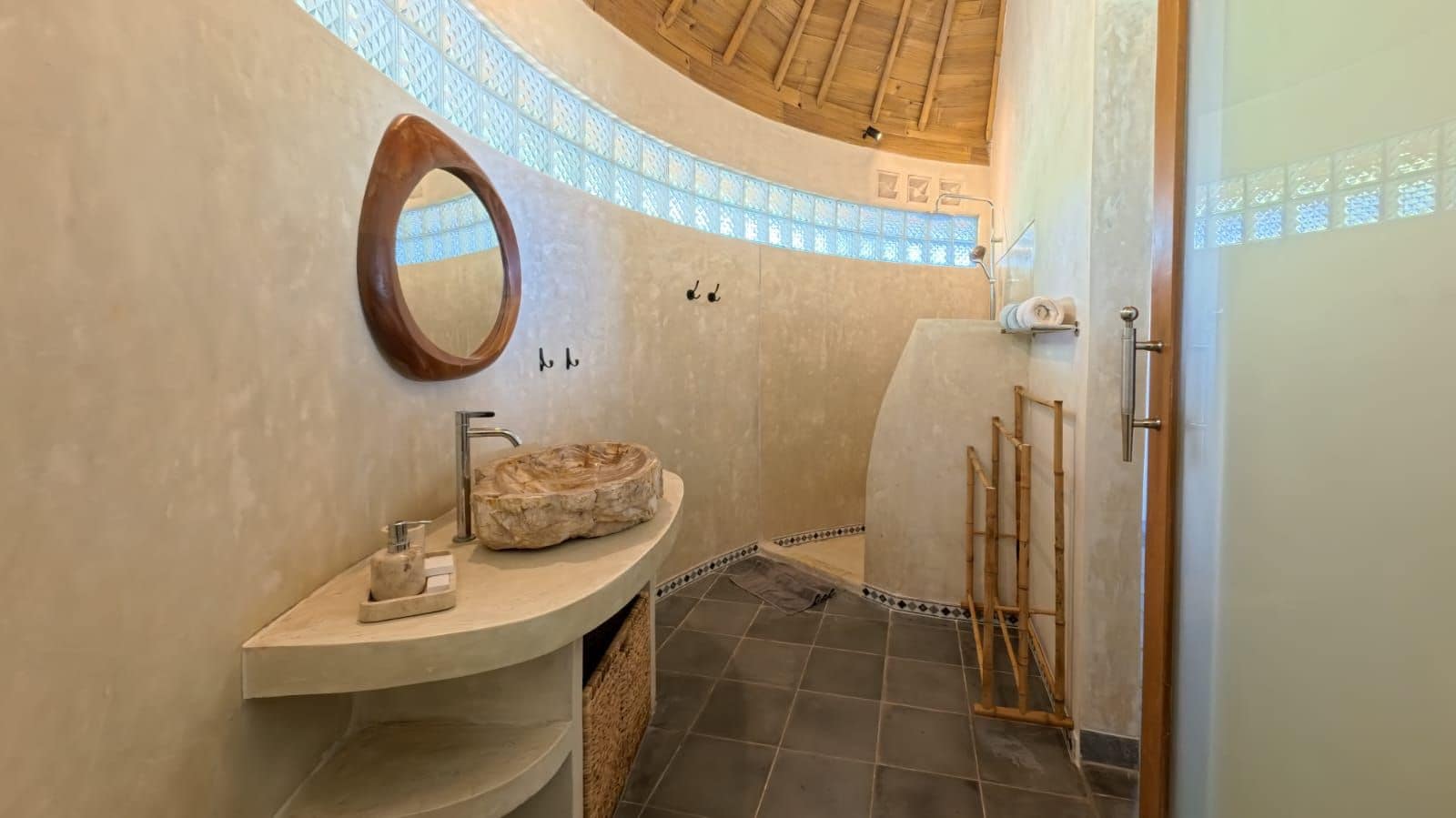 Une salle de bain avec un meuble-lavabo aux lignes courbes, un miroir rond, un lavabo en pierre et un espace douche.