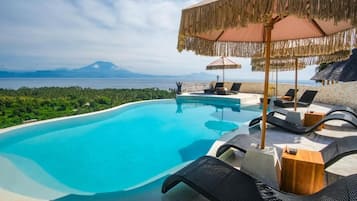 Piscina con sillas de descanso y sombrillas, con vistas a un paisaje montañoso.