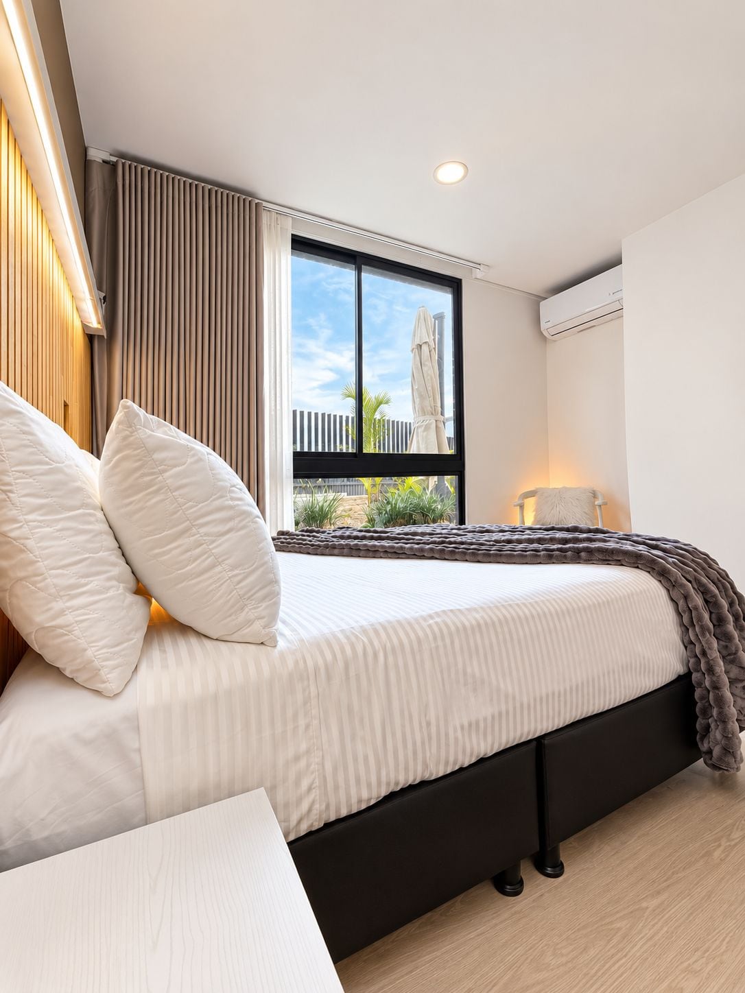 Un dormitorio moderno con una cama grande, una ventana con vistas al exterior y un equipo de aire acondicionado.