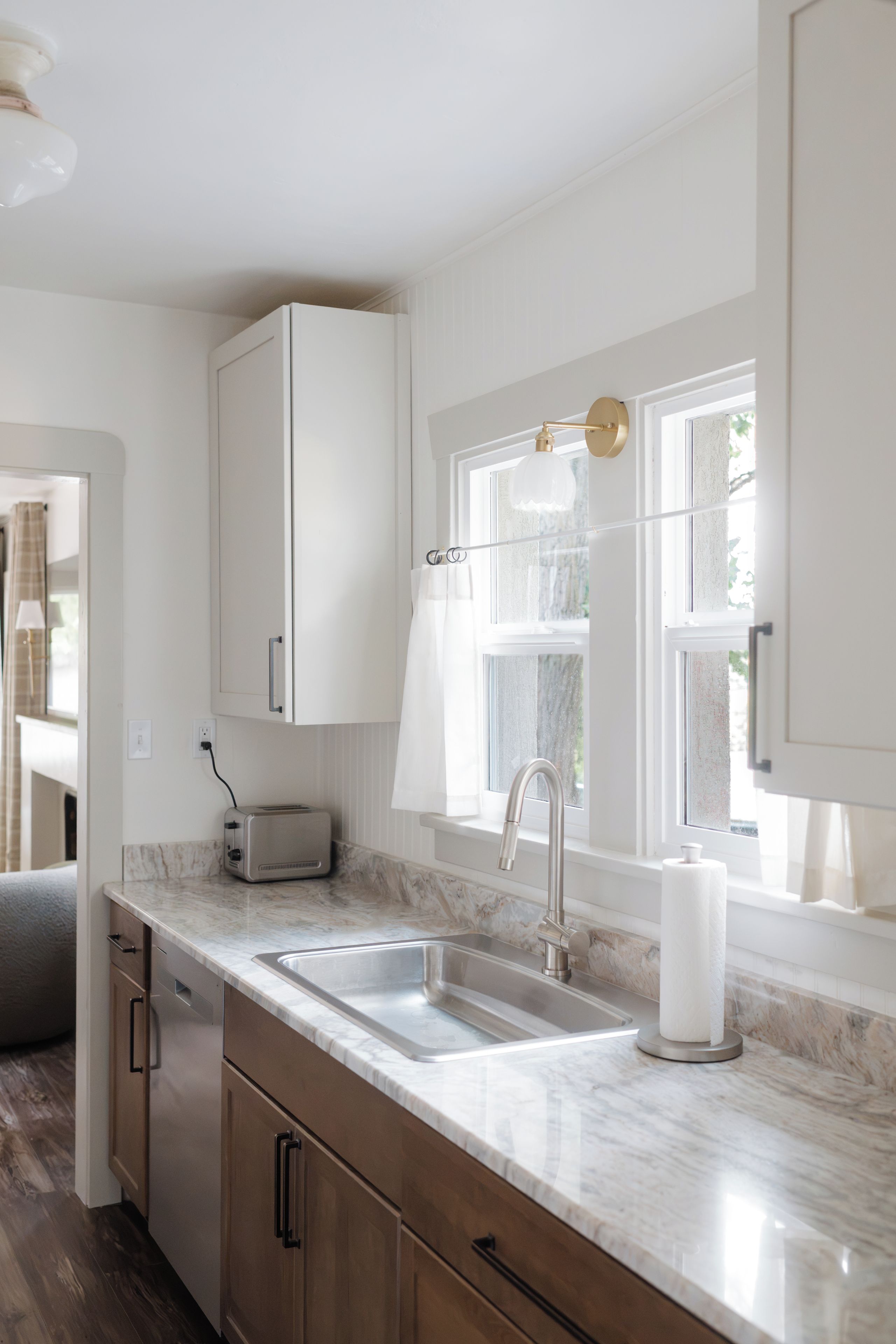 Una cocina moderna con muebles blancos, encimera de mármol, tostadora empotrada y ventana con vistas a zonas verdes.