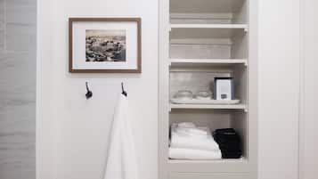 Ein Badezimmer mit einem weißen Handtuch an einem Haken, einem gerahmten Bild an der Wand und einem Ablagefach mit Handtüchern und einem Schild zur Entfernung von Make-up.
