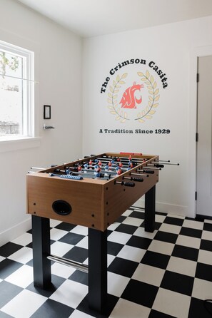 Een kamer met een tafelvoetbaltafel, een zwart-wit geruite vloer en een muur met een logo en tekst.