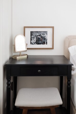 Een klein kaptafeltje met spiegel en een lijst met een foto aan een muur.