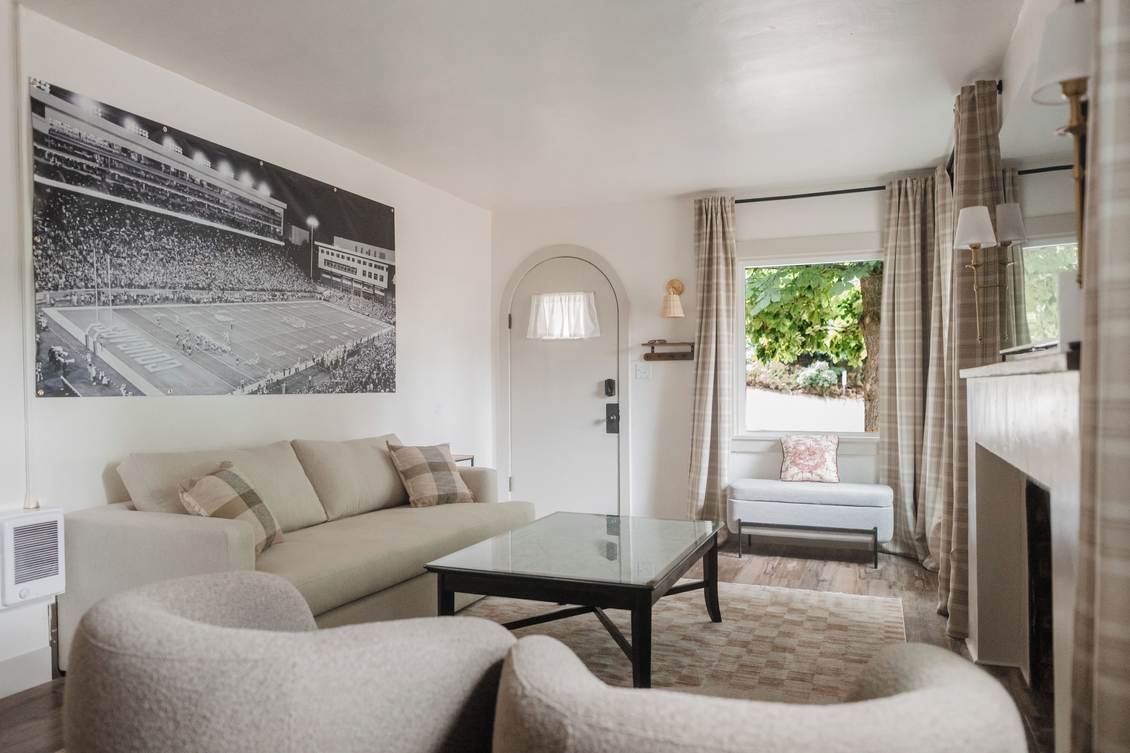 Ein Wohnzimmer mit einer Couch, Sesseln, einem Couchtisch, einem großen Bilderrahmen, einem Kamin und Blick ins Grüne.