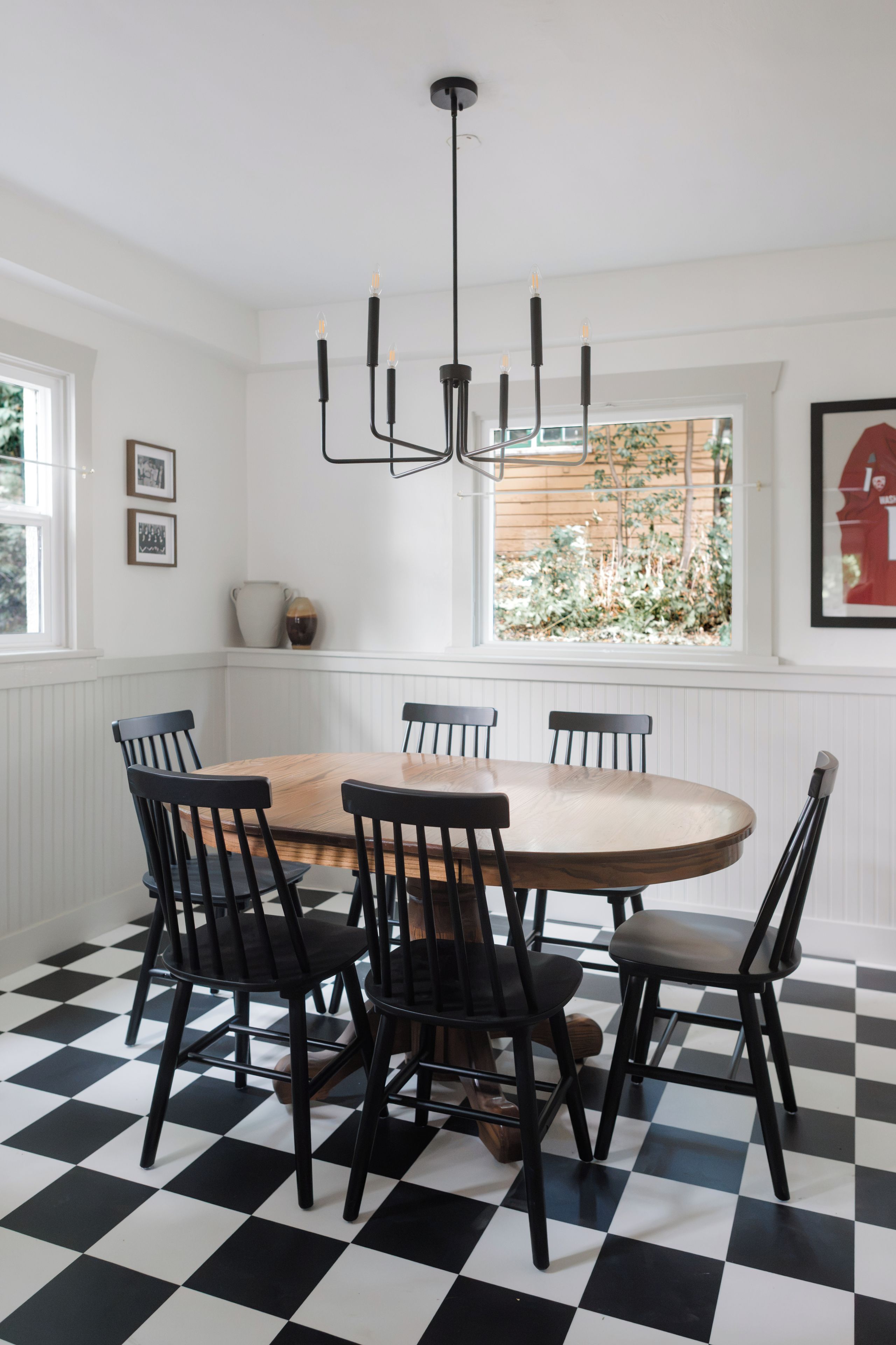 A dining area with a round table surrounded by chairs, a black and white checkered floor, and a pendant light fixture.