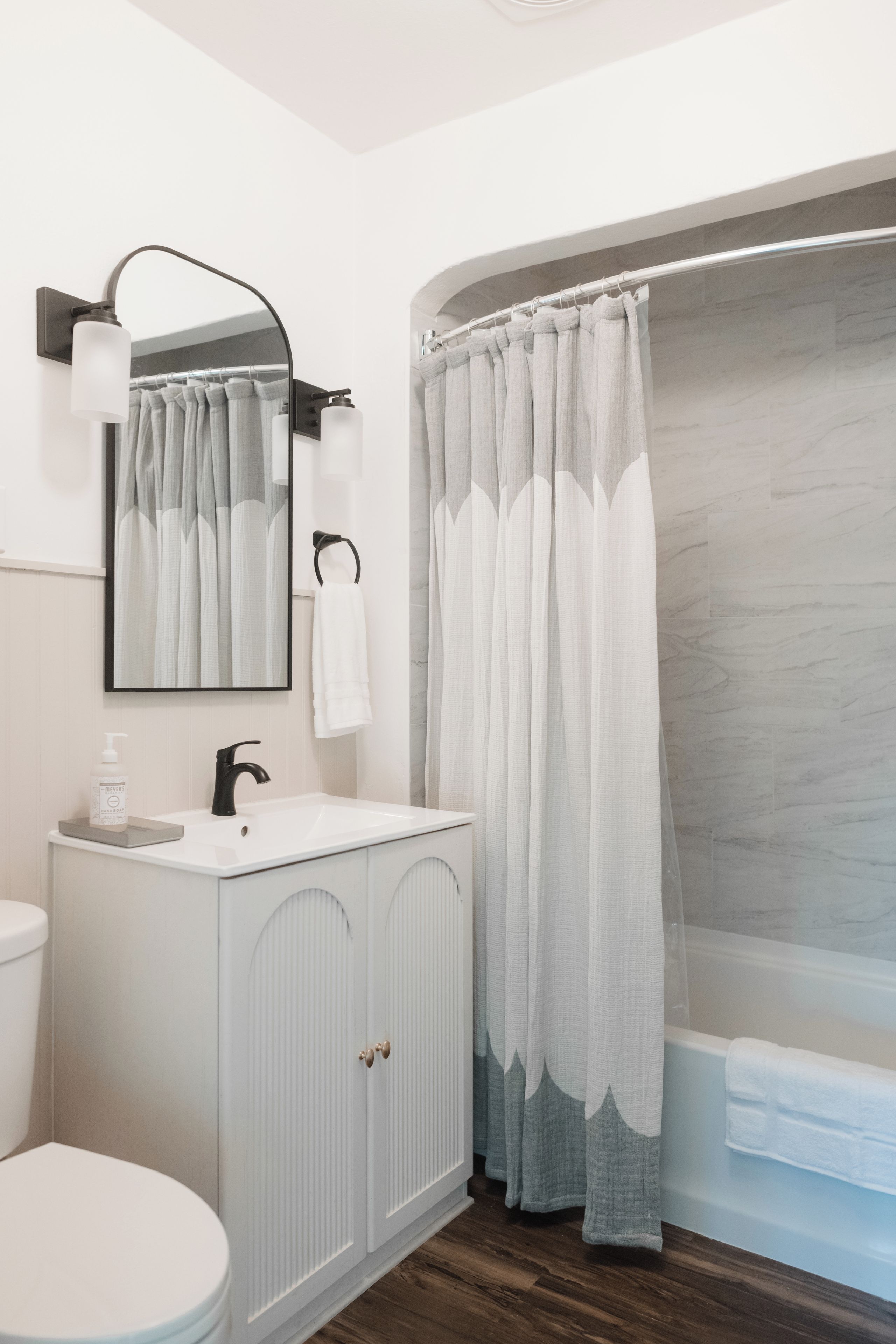 Un baño con tocador blanco, un espejo, toallero, cortina de ducha y bañera.