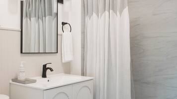 Un baño con tocador blanco, un espejo, toallero, cortina de ducha y bañera.