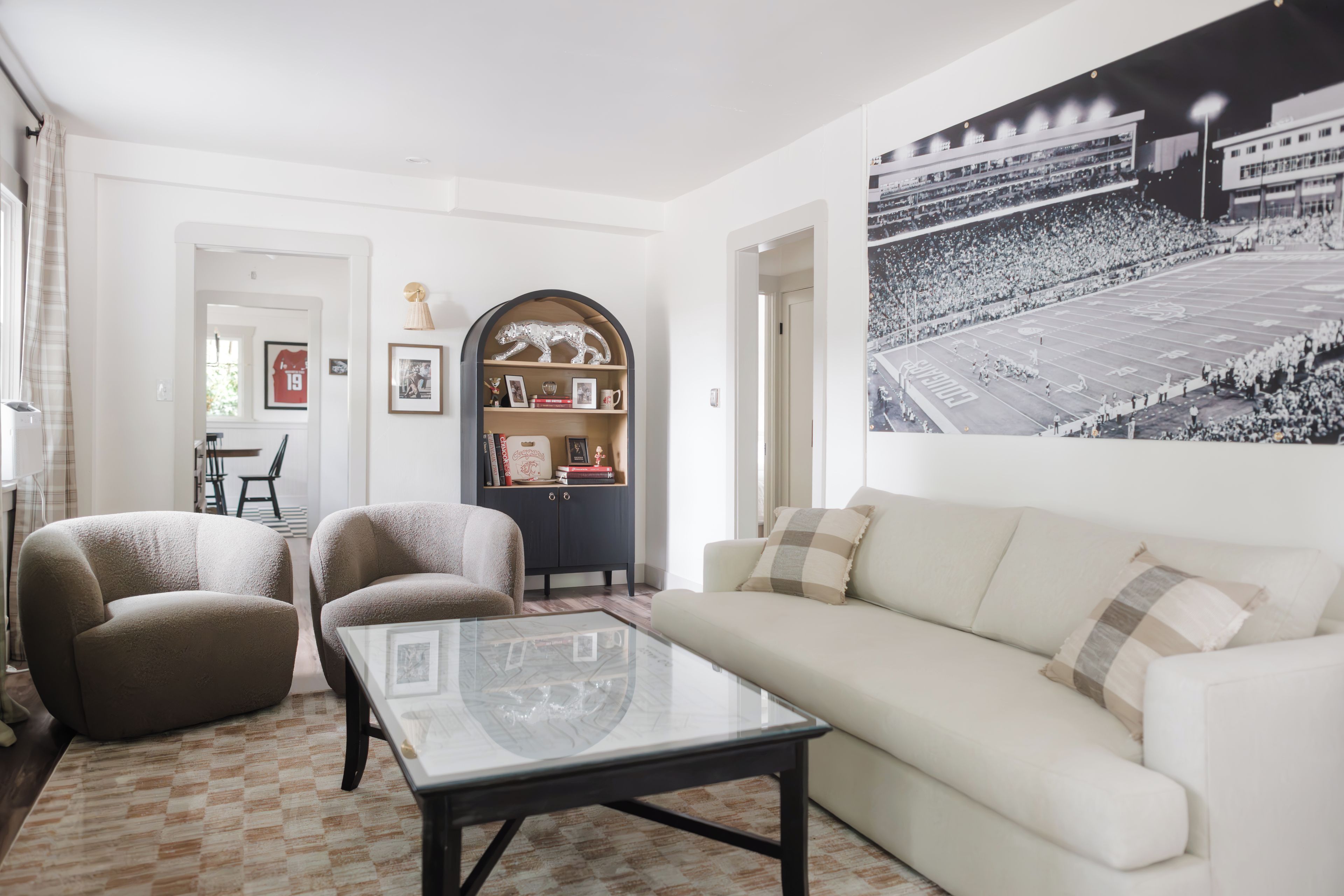 Una sala de estar con un sofá, sillones, una mesita de centro y una estantería con fotos enmarcadas y objetos decorativos.