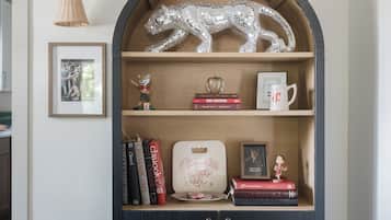 Une bibliothèque en bois foncé, de forme arquée, surmontée d’une figurine d’animal avec une surface miroitante, ainsi que de livres, un tableau encadré et une tasse.