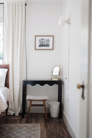Un baño pequeño con un banco de madera, un cubo de basura blanco, un cuadro en la pared y un espejo sobre un mueble consola.