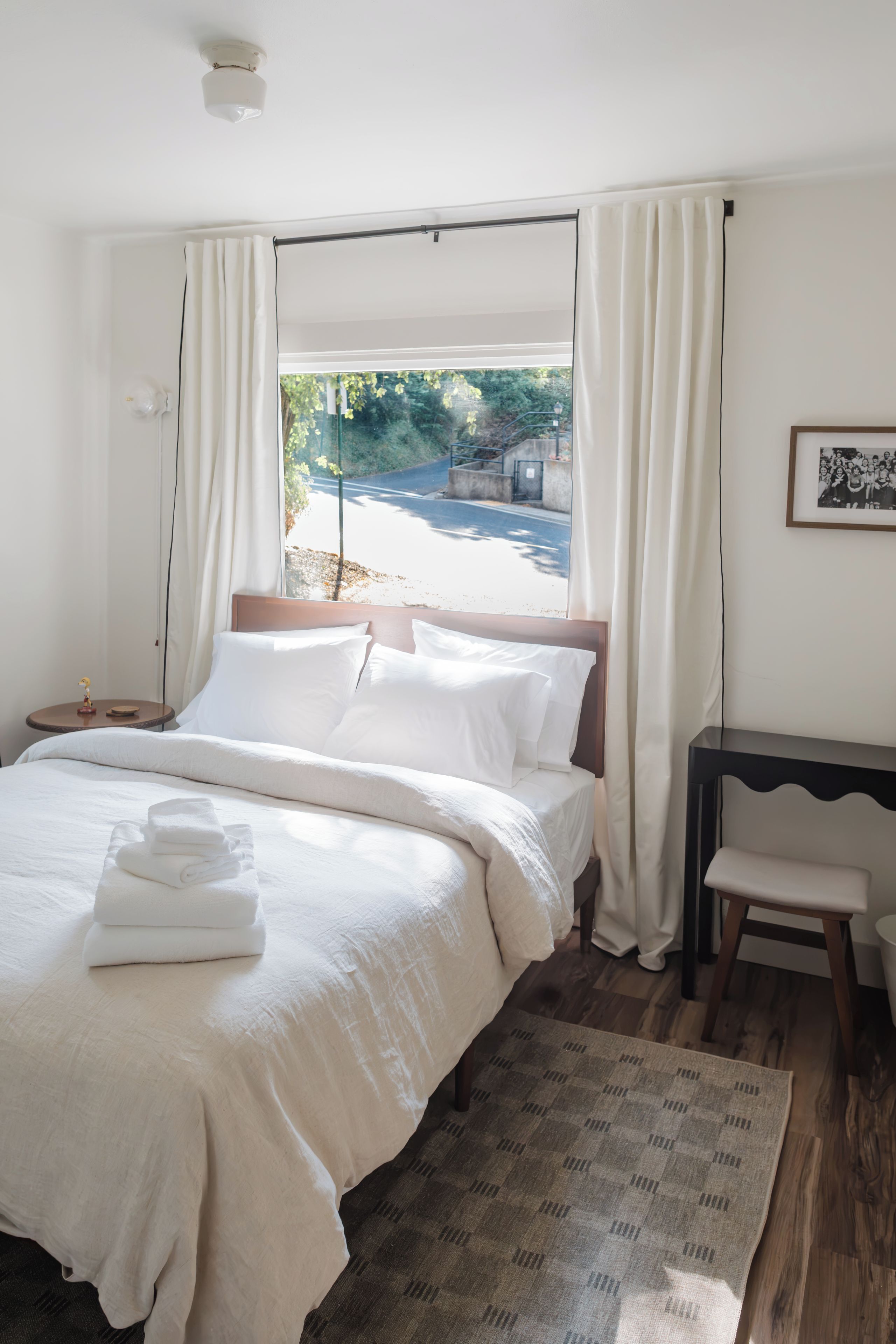 A bedroom with a large bed, a bedside table, a chair, a rug, and a window with curtains.