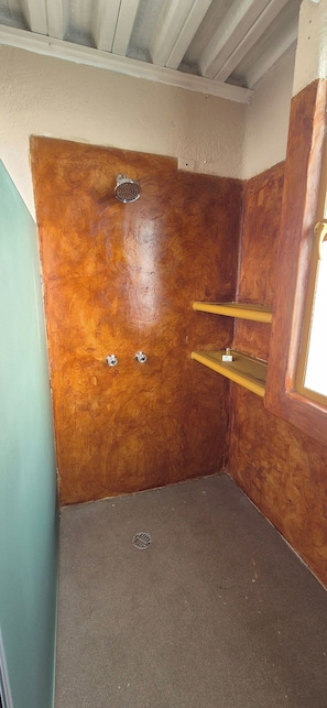 Un baño pequeño y cerrado con pared de madera, ducha y un estante sencillo.