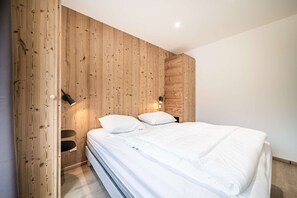 A bedroom with a wooden panel wall, a bed with white bedding, and two wall-mounted lamps. - JANIN 5 Charming renovated apartment 1 bedroom + cabin (MORZINE)