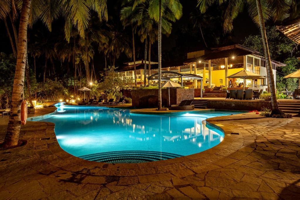 A nighttime swimming pool area with a curved design, surrounded by palm trees and a building with outdoor seating.