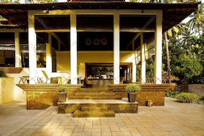 A building with a stone facade, multiple windows, and a covered entrance area with steps leading up to it. - coconut creek resort (Marmagao)