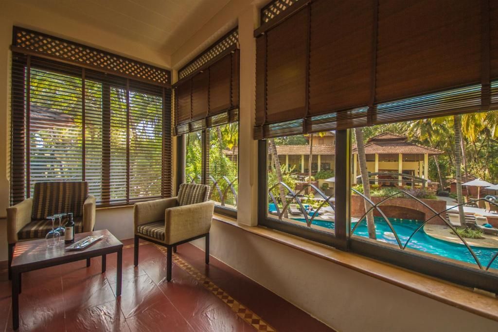 A room with a pool view, large windows with blinds, a sofa, and a coffee table.