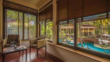 A room with a pool view, large windows with blinds, a sofa, and a coffee table.