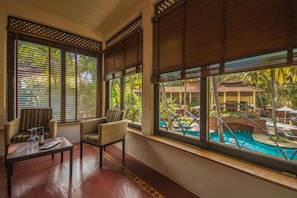 A room with a pool view, large windows with blinds, a sofa, and a coffee table. - coconut creek resort (Marmagao)