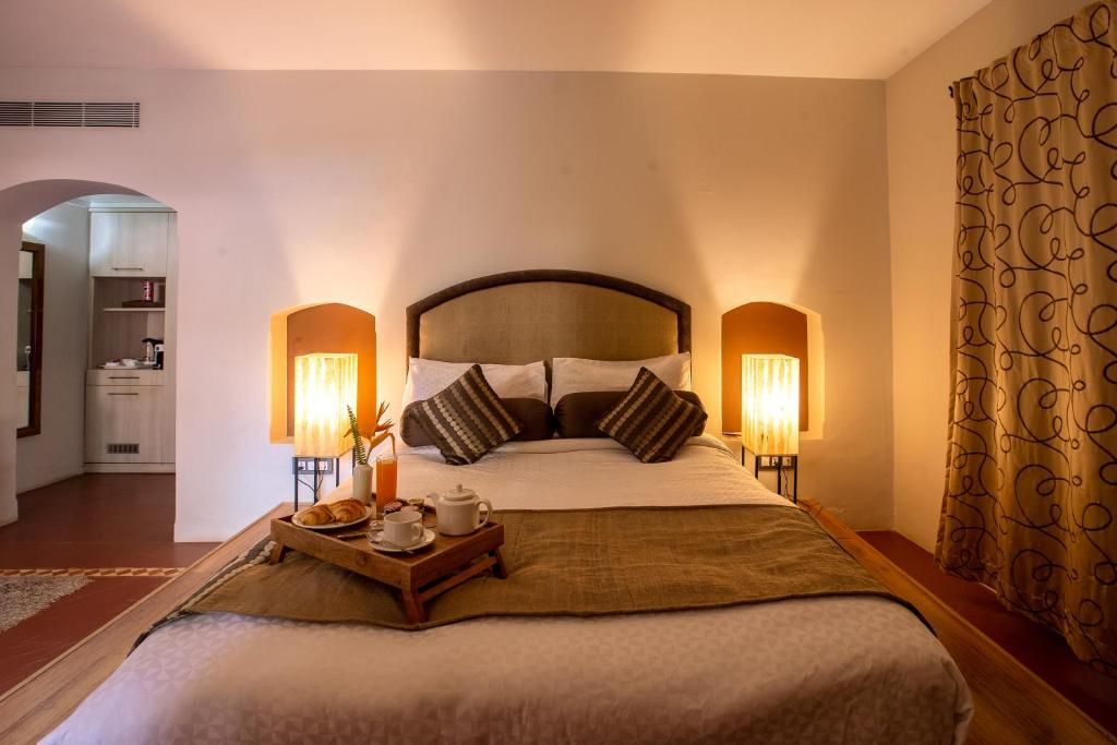 A hotel room with a large bed, two bedside lamps, a tray with breakfast items, and a view of the hallway.