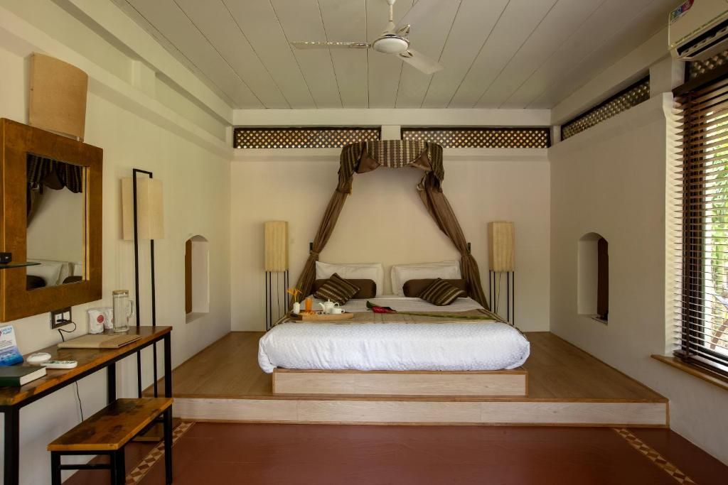 Een slaapkamer met een hemelbed, nachtkastjes, een spiegel en een raam met jaloezieën.