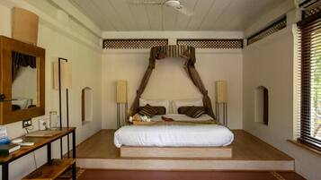 Een slaapkamer met een hemelbed, nachtkastjes, een spiegel en een raam met jaloezieën.
