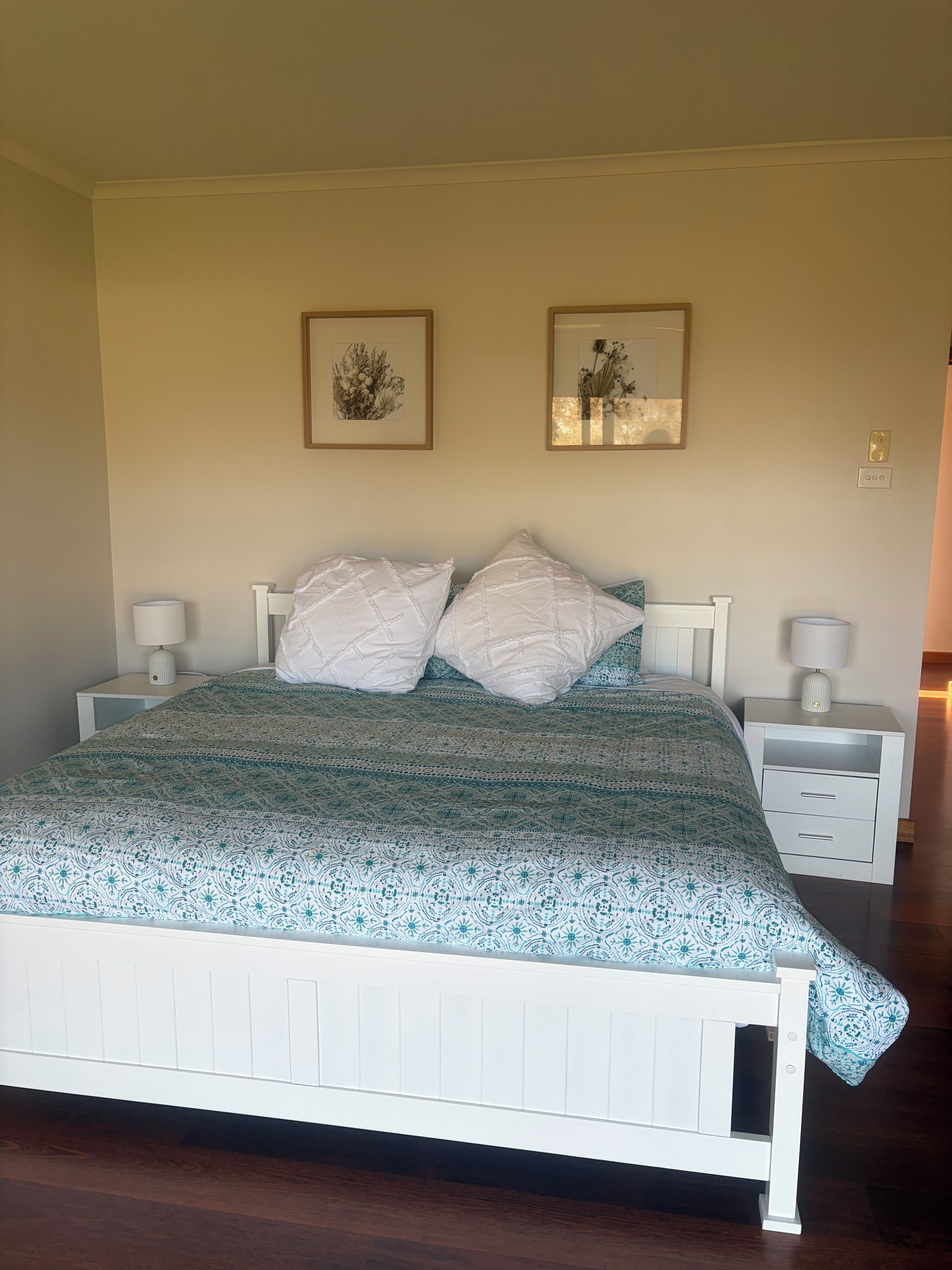 A bed with a patterned bedspread, two pillows, two bedside tables with lamps, and two framed pictures on the wall.