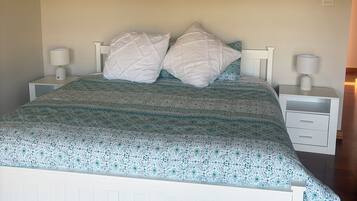 A bed with a patterned bedspread, two pillows, two bedside tables with lamps, and two framed pictures on the wall.