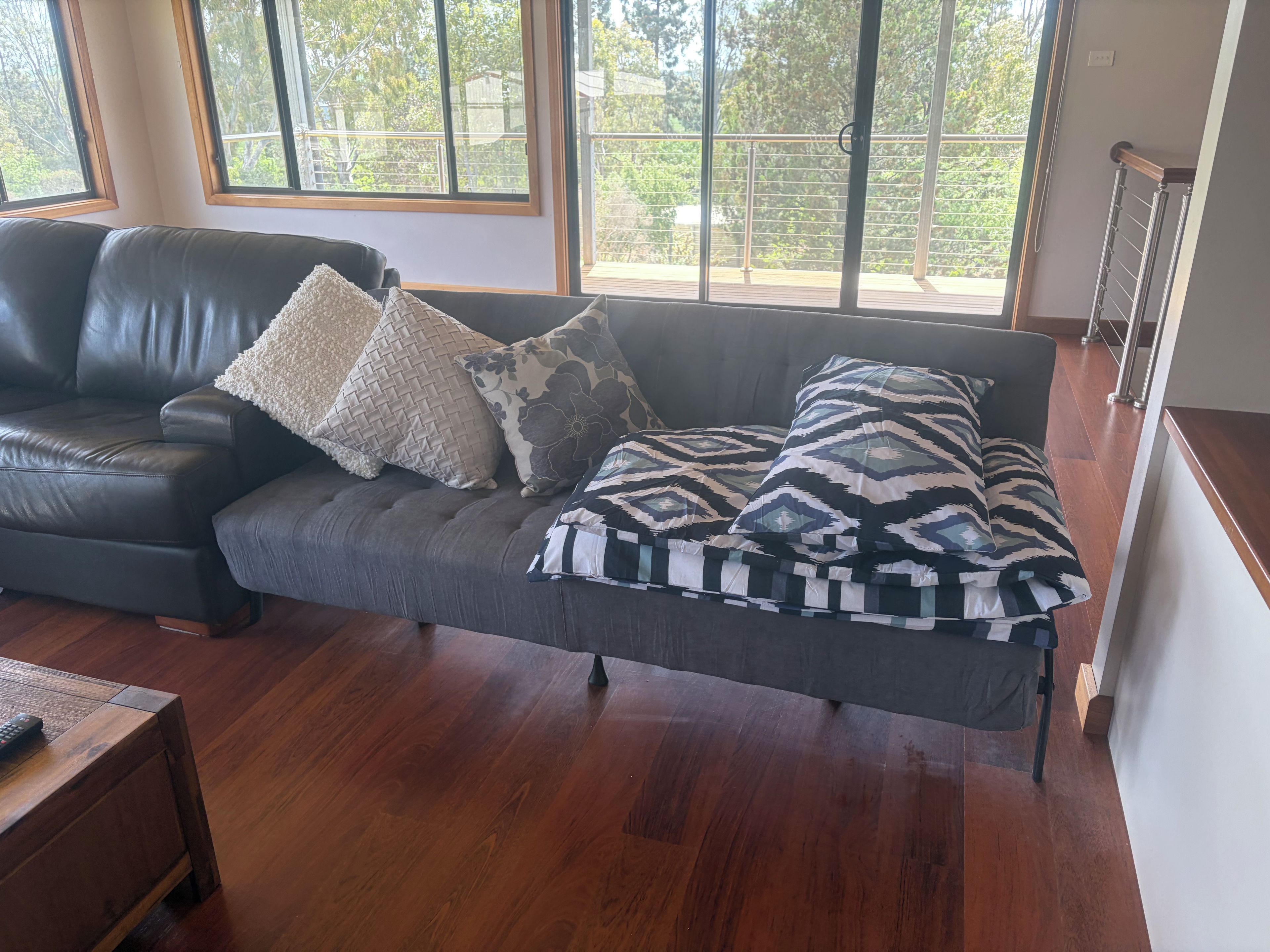 A modern living room with a dark leather sofa, patterned cushions, and a wooden coffee table.