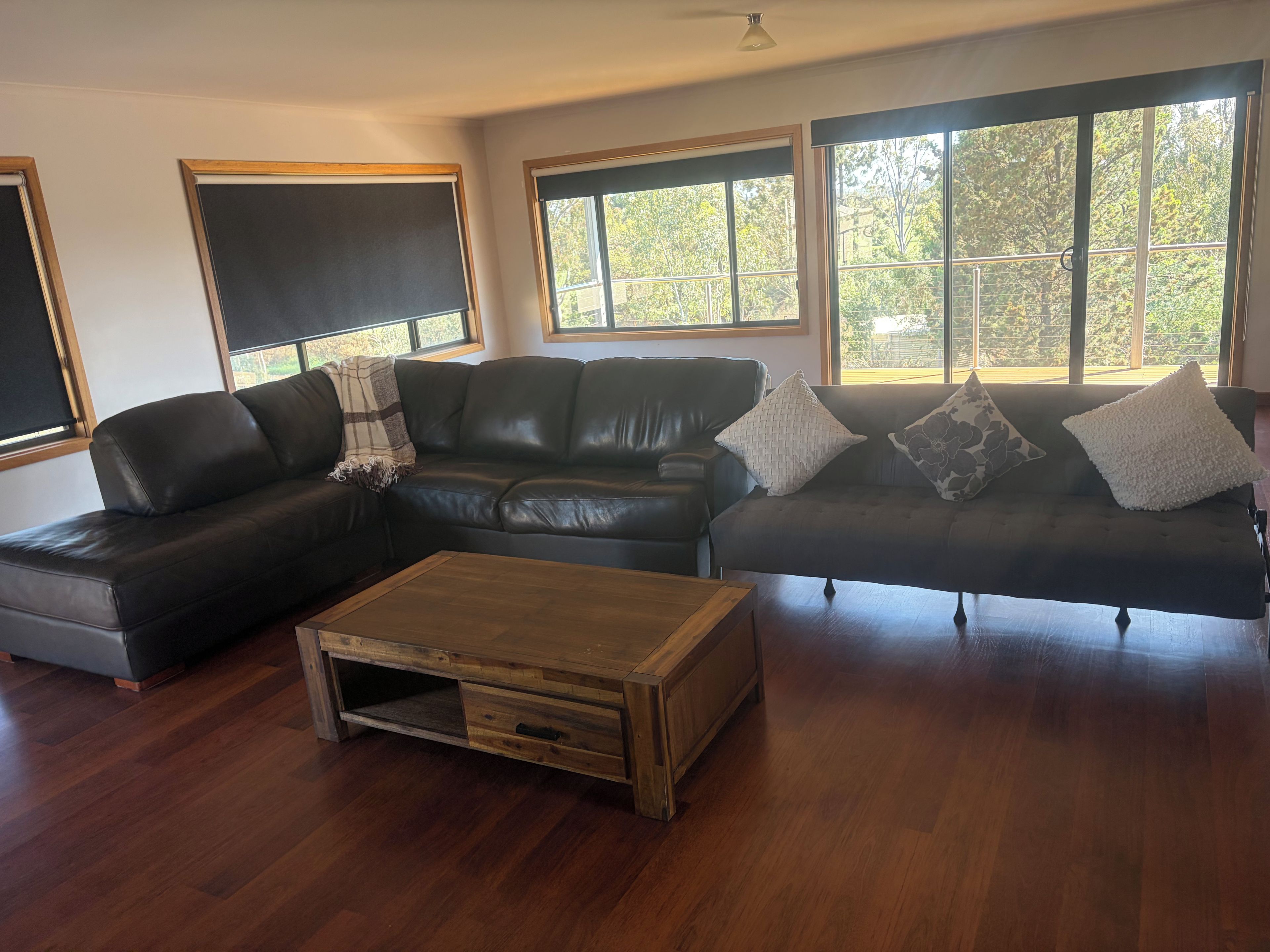 A living room with a sectional sofa, a wooden coffee table, and large windows with a view of trees.