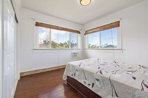 Ein Schlafzimmer mit einem Bett, zwei Fenstern mit Bambusrollos, einem Holzboden und einer weißen Decke.