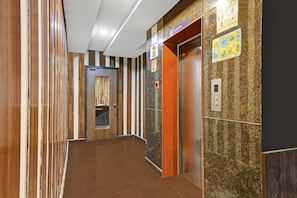 En gang med væg af træpaneler, en elevator og en dør med gardin.