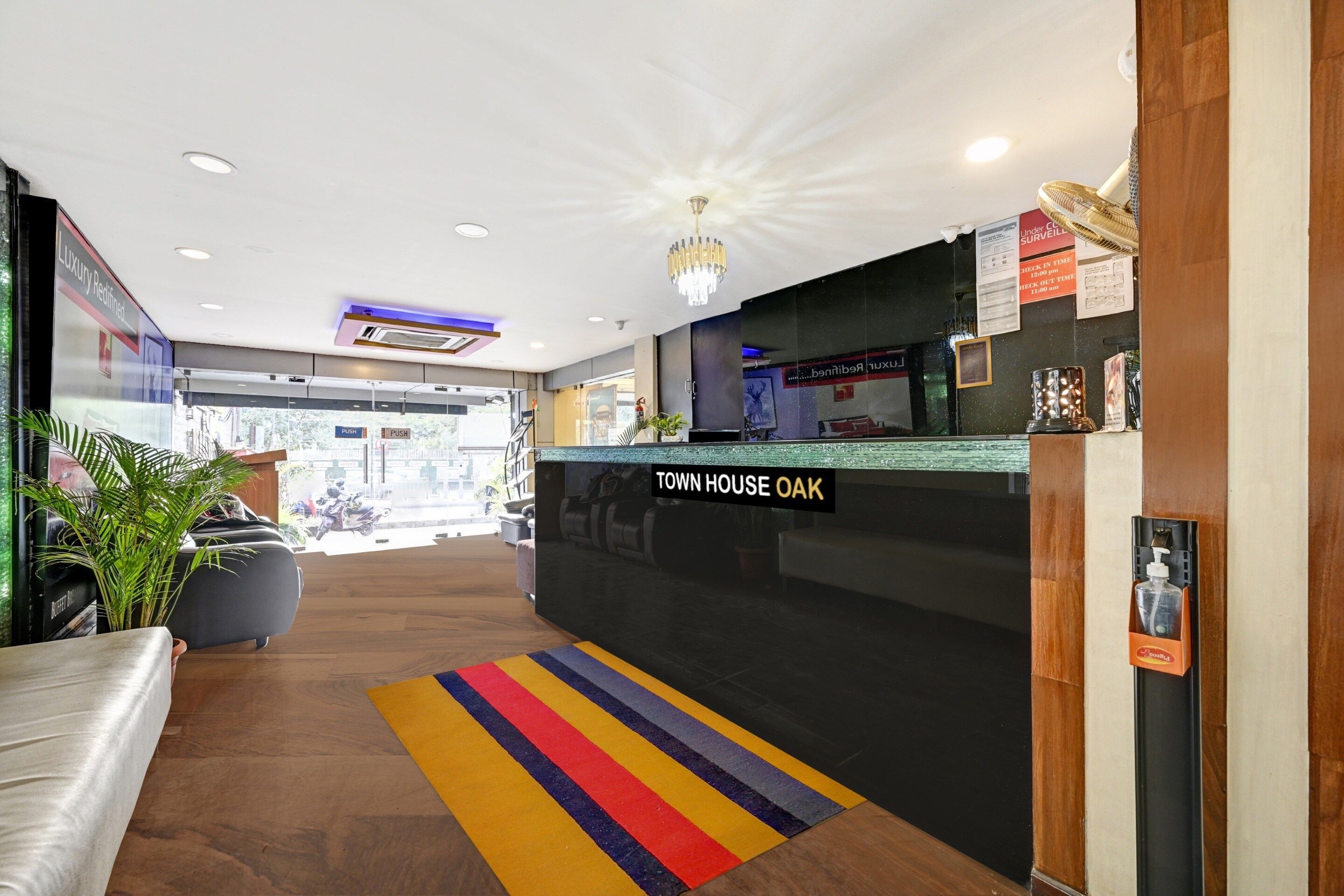 A hotel reception area with a 'Town House Oak' sign, a reception desk, a colorful striped rug, and a potted plant.
