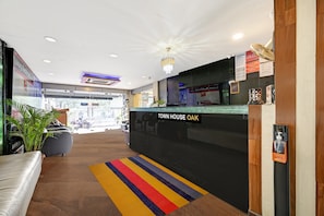 A hotel reception area with a 'Town House Oak' sign, a reception desk, a colorful striped rug, and a potted plant. - Townhouse OAK Hotel Berrys (Bangalore)