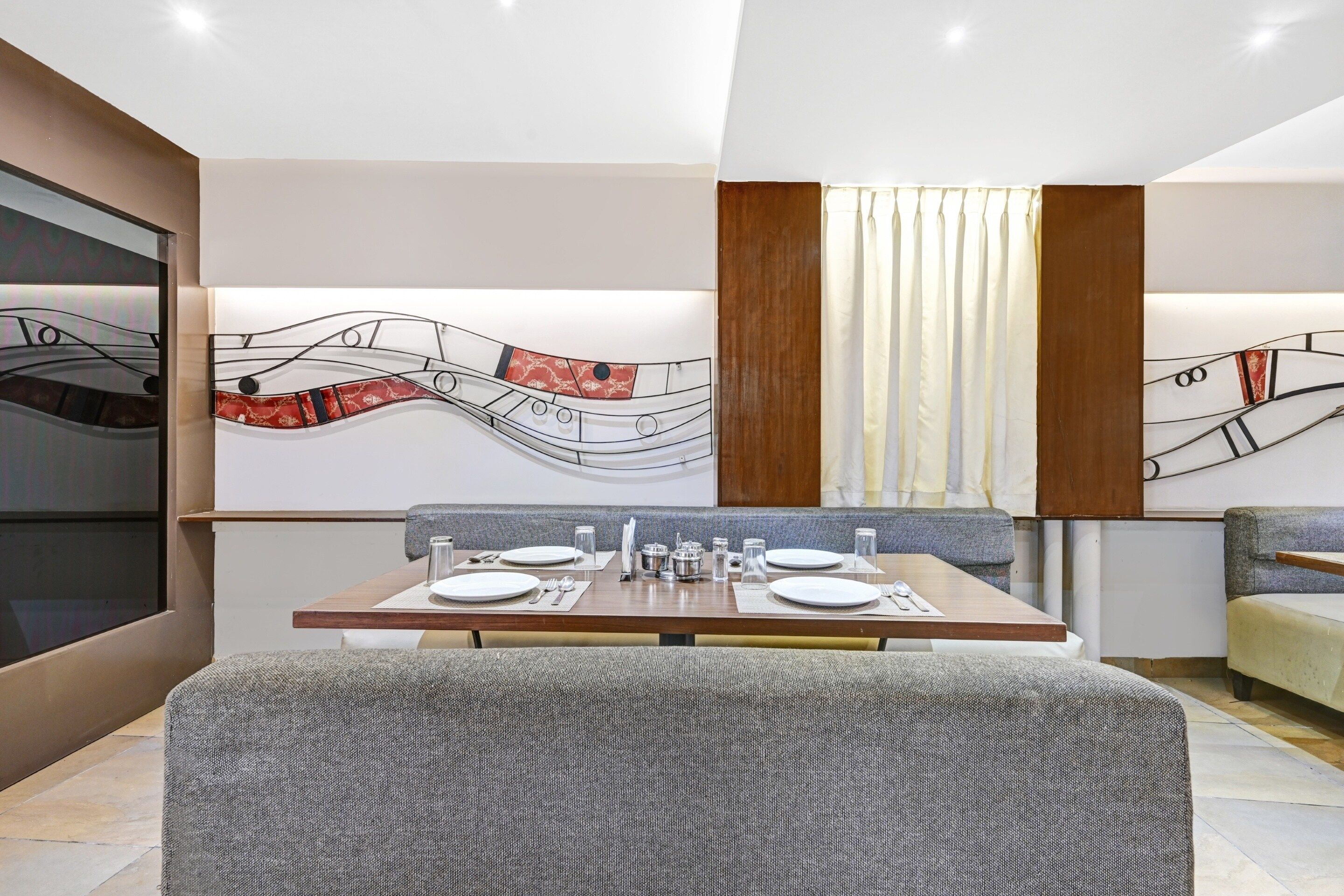 A modern dining area with a long table set for two, a patterned wall, and a large window with curtains.