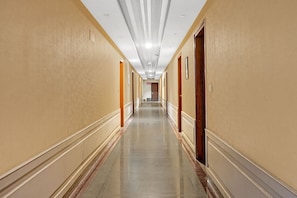 Un pasillo largo y estrecho en un hotel, con puertas a ambos lados, piso de baldosas brillantes e iluminación empotrada en el techo.